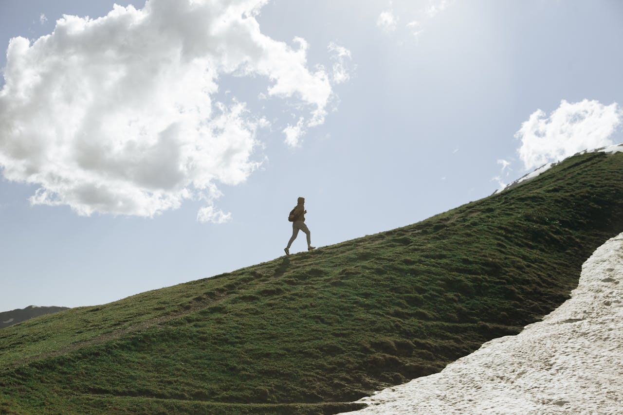 A person hiking on a grassy hill with a clear sky and clouds overhead, embodying adventure.