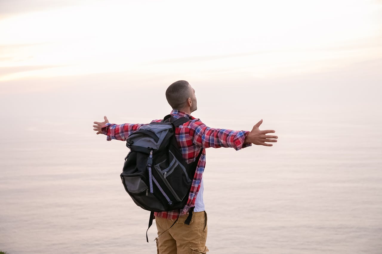 A man in plaid exploring a scenic ocean view with arms outstretched in a sense of freedom.