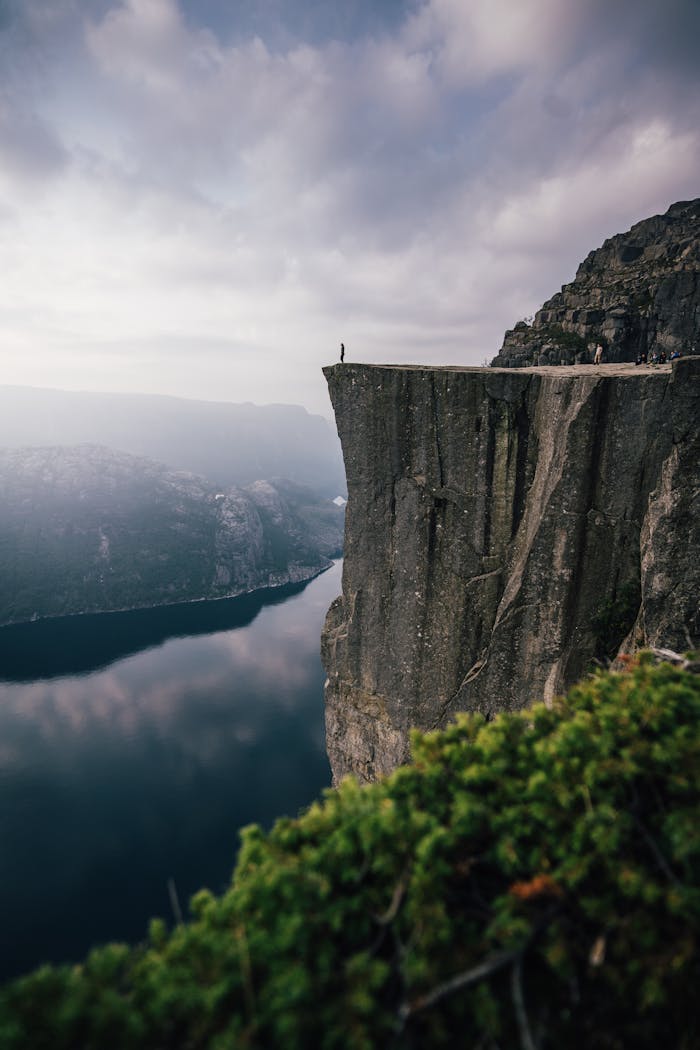 A lone adventurer stands on the edge of Preikestolen cliff, overlooking the stunning fjord below in Norway.
